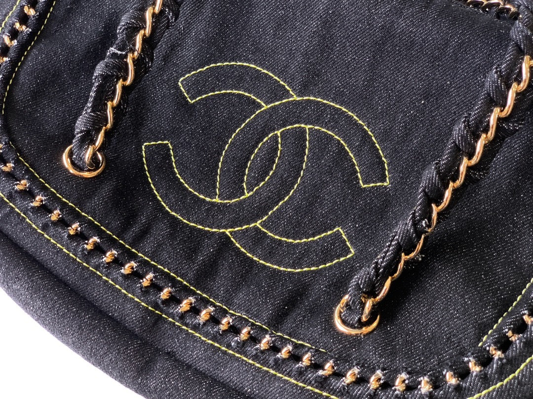 Close-up of a black denim shoulder bag featuring a prominent yellow embroidered interlocking CC logo, gold-tone chain strap details, and contrast yellow stitching.