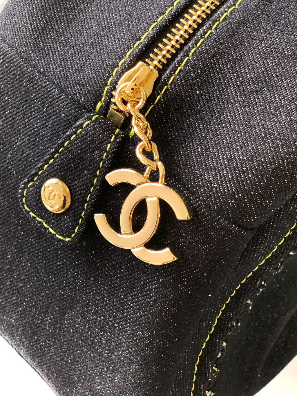 Close-up of a black textured fabric bag with gold zipper, gold stitching, and a gold-tone interlocking CC charm on a chain.