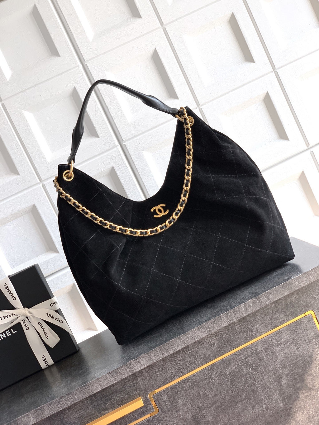 Black quilted handbag with gold chain detail on a white geometric background