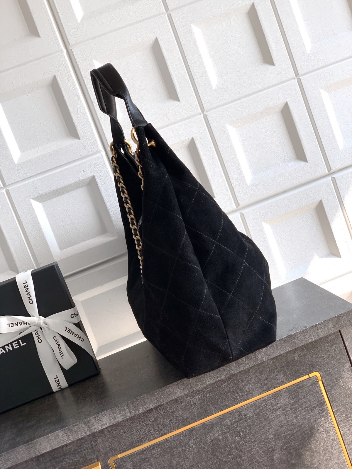 Black quilted handbag with gold chain on a gray surface with Chanel boxes in the background.