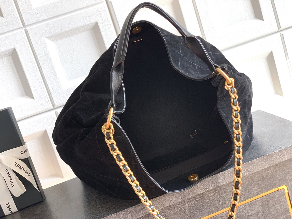 Black handbag with gold chain strap on a textured surface