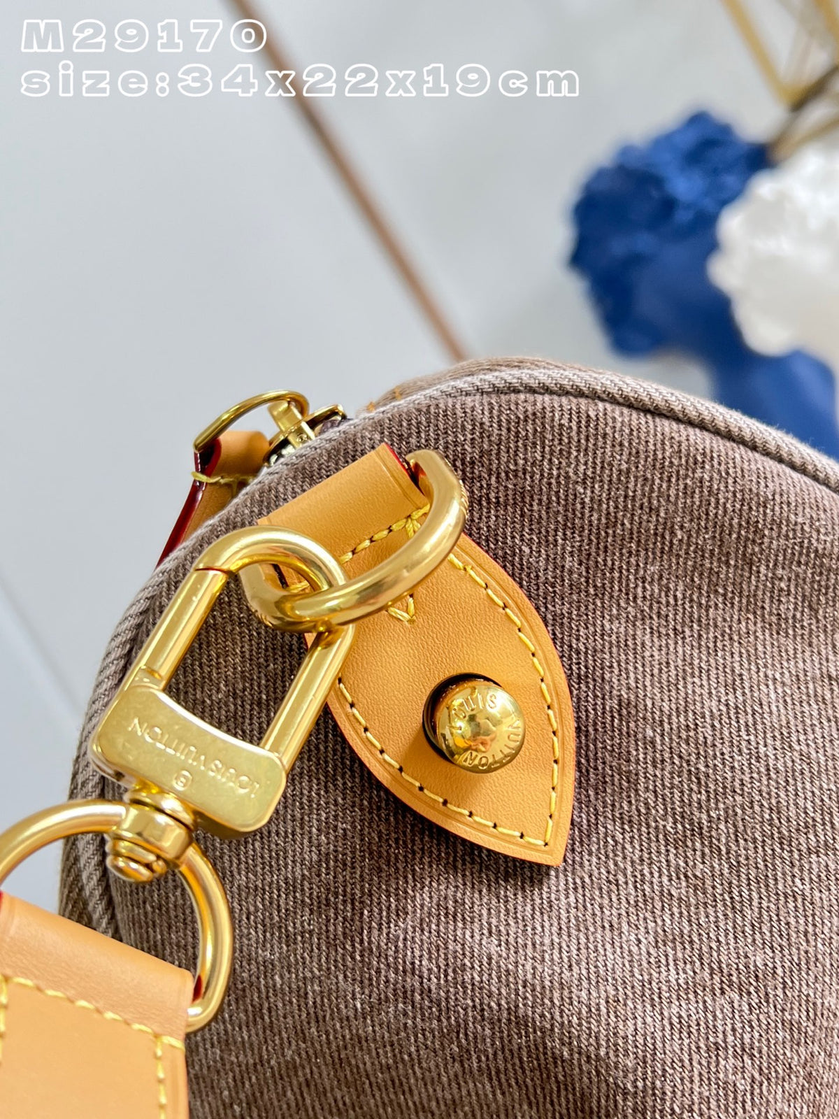 Close-up of a brown woven fabric bag with a tan leather strap tab and gold-tone hardware, including a D-ring clasp engraved with 'Nagasaki' and a round snap button.