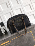 A black denim shoulder bag with gold-tone hardware, featuring a prominent interlocking CC logo on the front and a braided chain handle, displayed on a dark gray cabinet against a white tiled wall.
