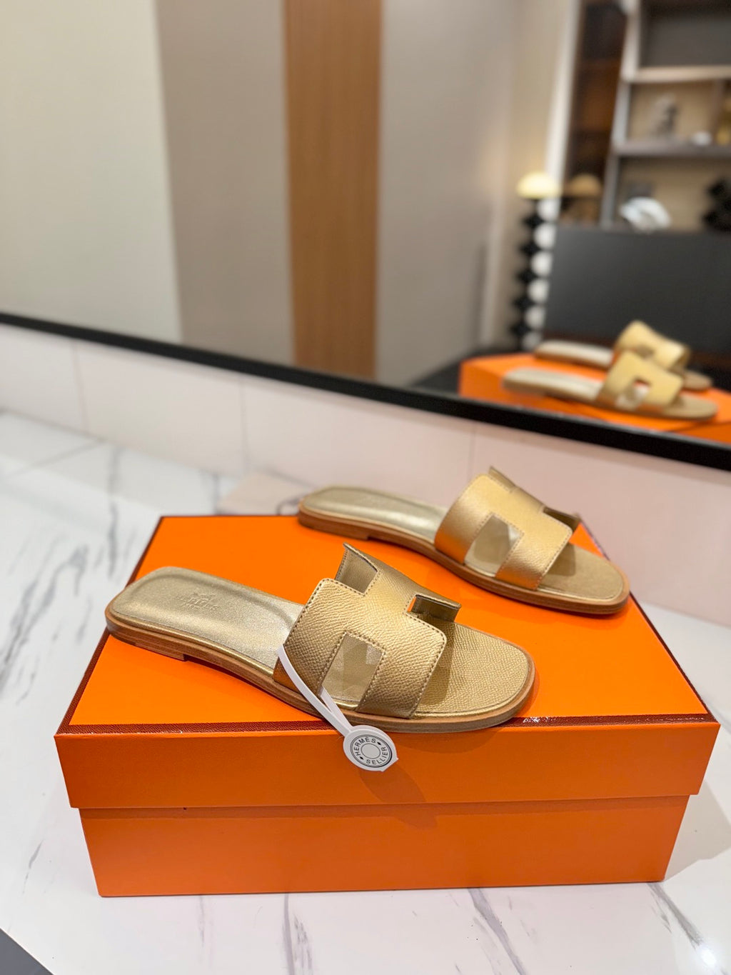 Gold sandals on an orange box with a mirror reflecting the scene