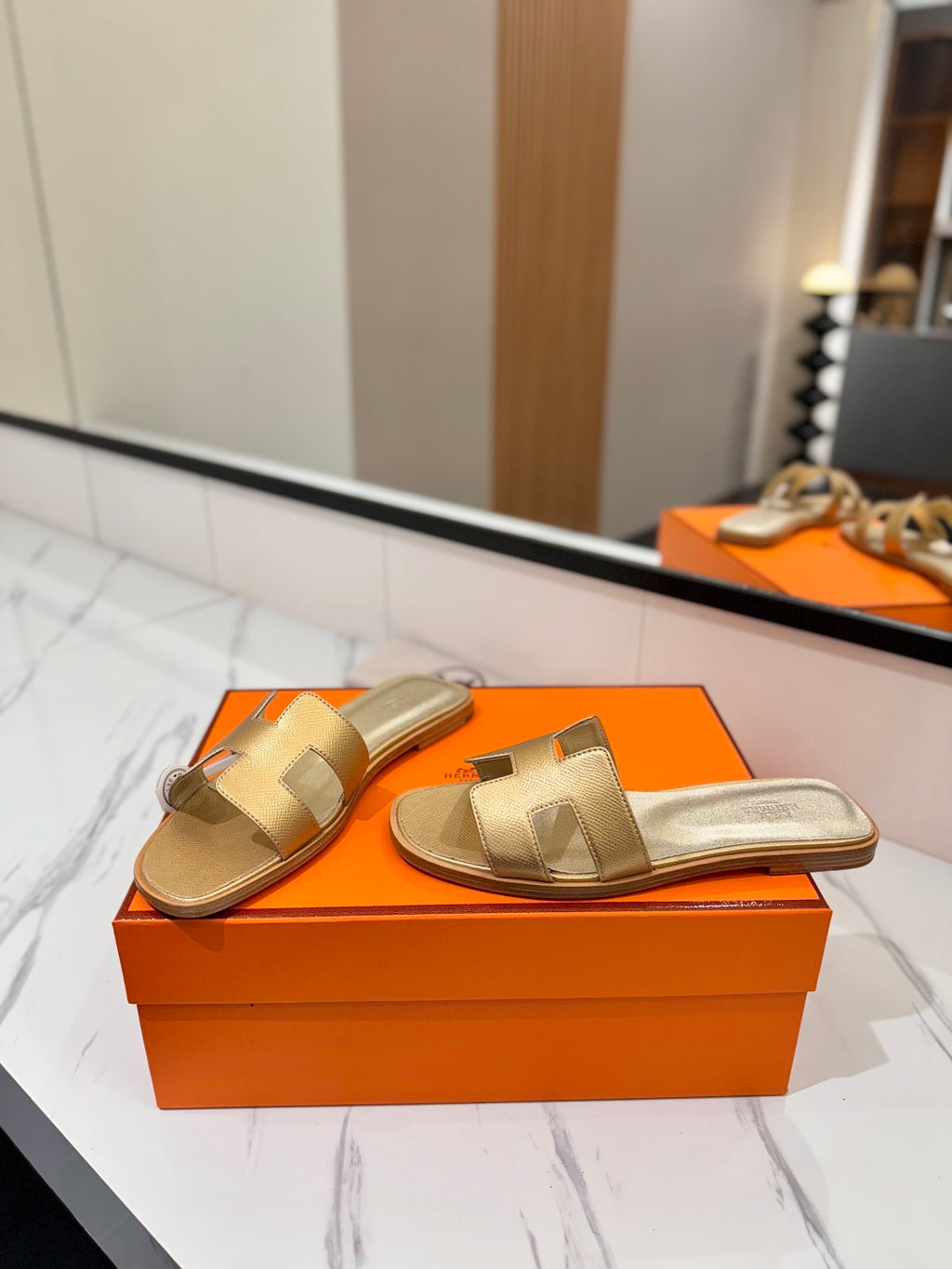 Gold sandals on an orange box with a mirror reflection in the background