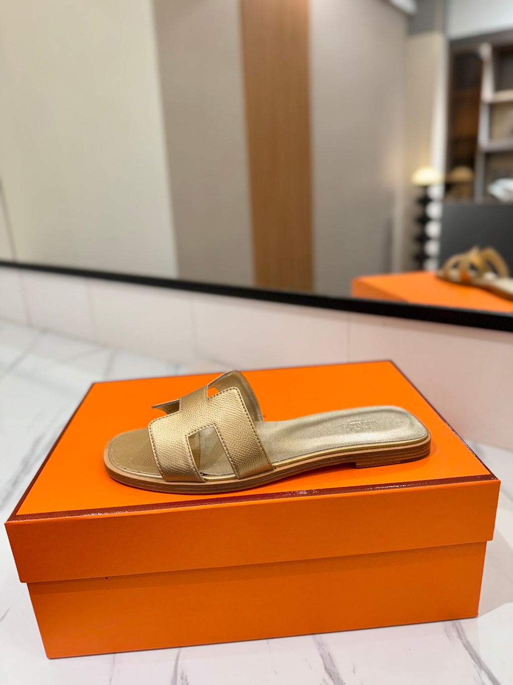 Gold sandal on an orange box with a blurred indoor background