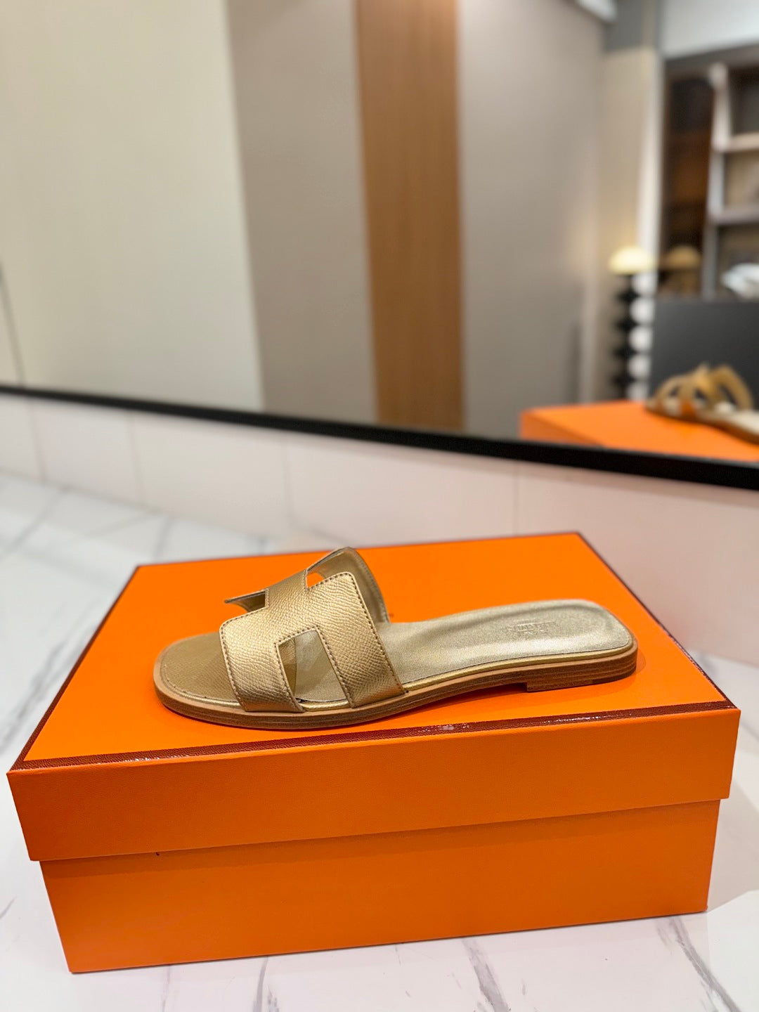 Gold sandal on an orange box with a blurred indoor background