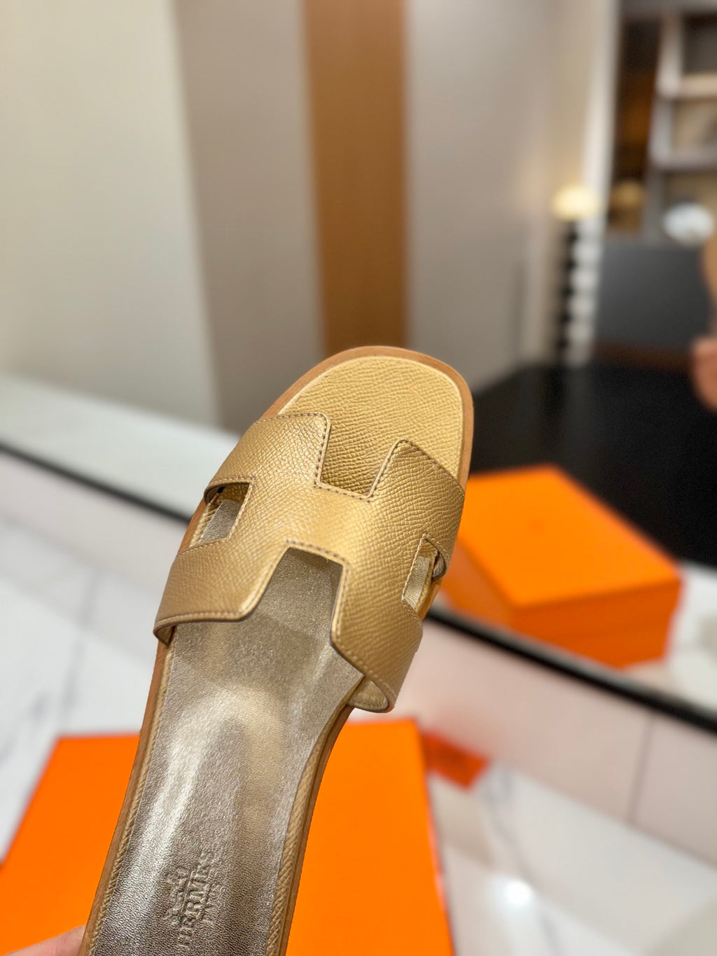 Gold sandal with a brand logo on an orange box