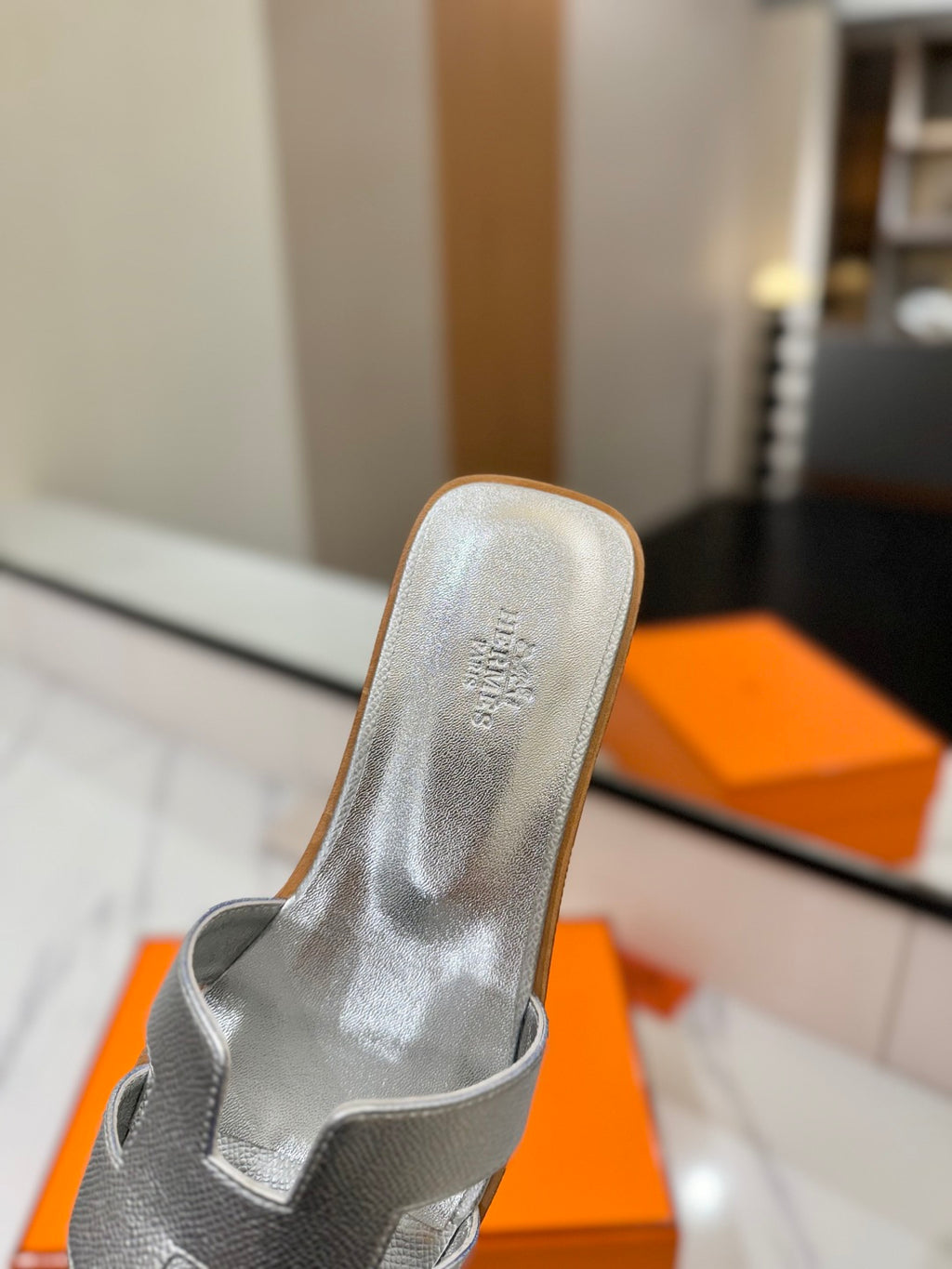 Silver sandal with brand logo on a blurred indoor background