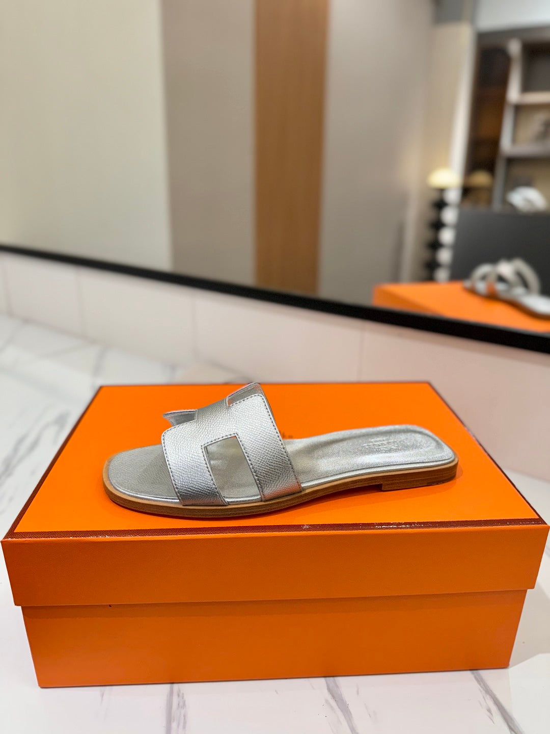 Silver sandal on an orange box with a blurred indoor background