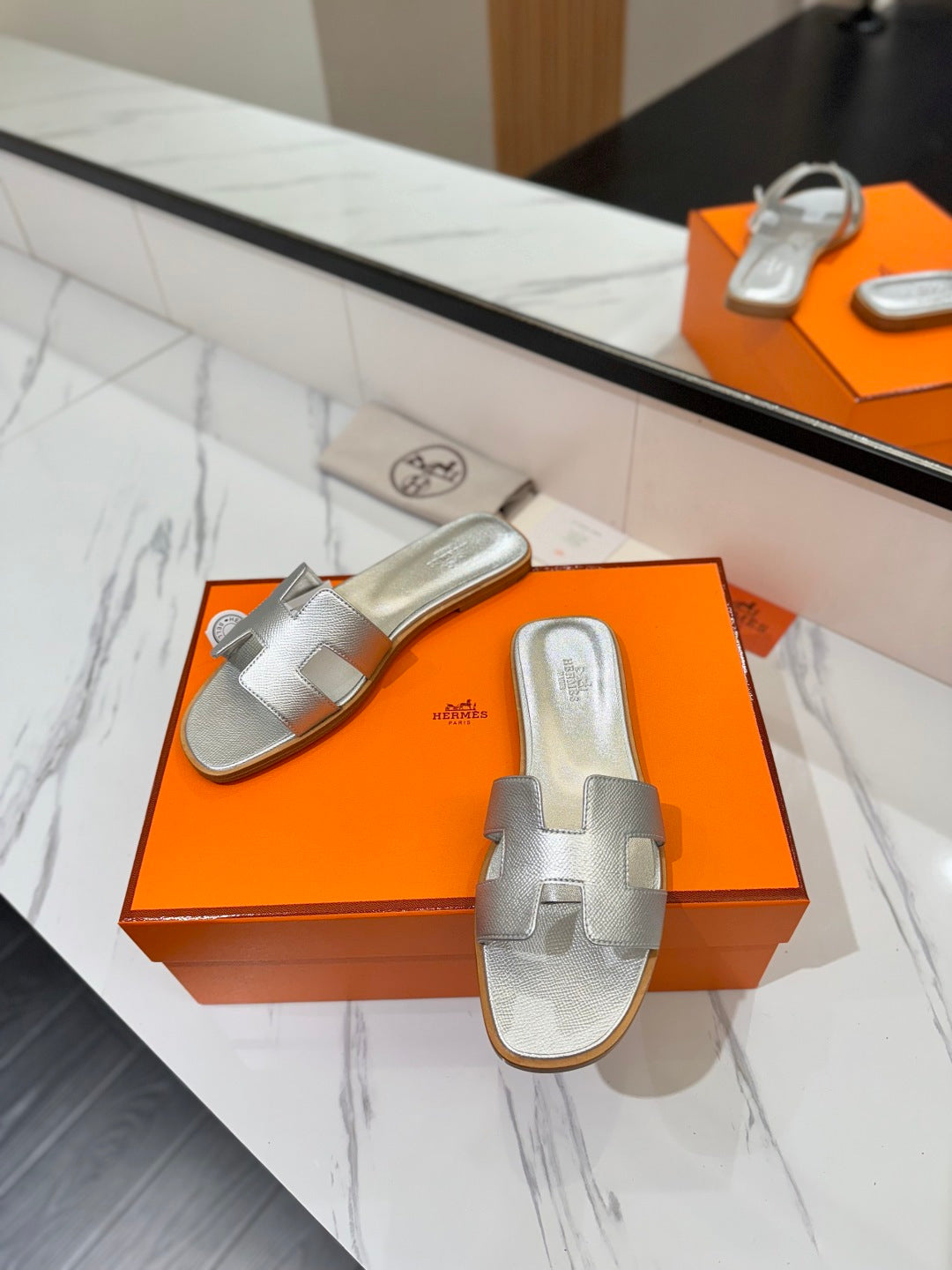 Silver sandals on an orange box with a reflective surface in the background