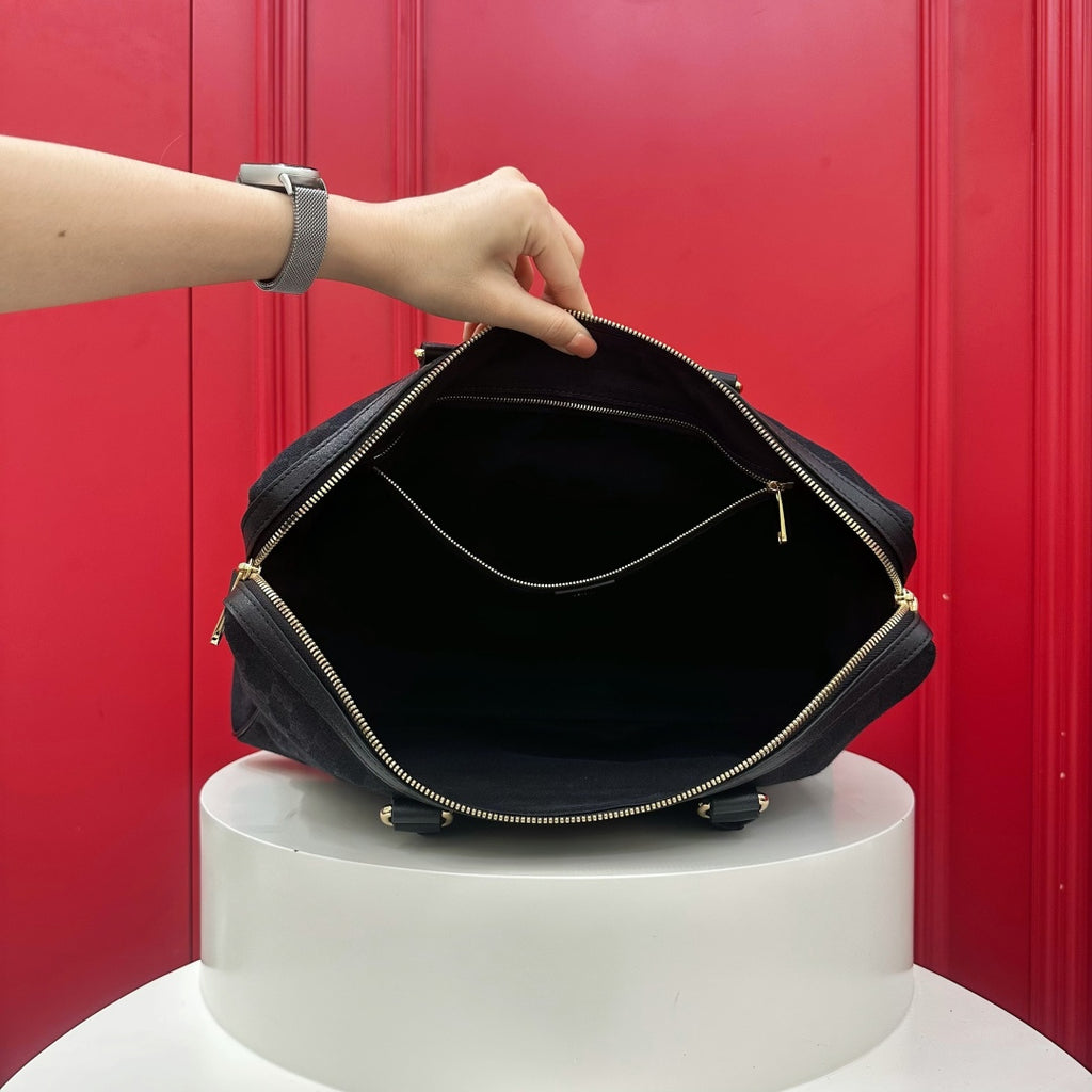 A black nylon shoulder bag with gold-tone zippers is shown open, held by a person's hand on a white pedestal in front of a red paneled background.