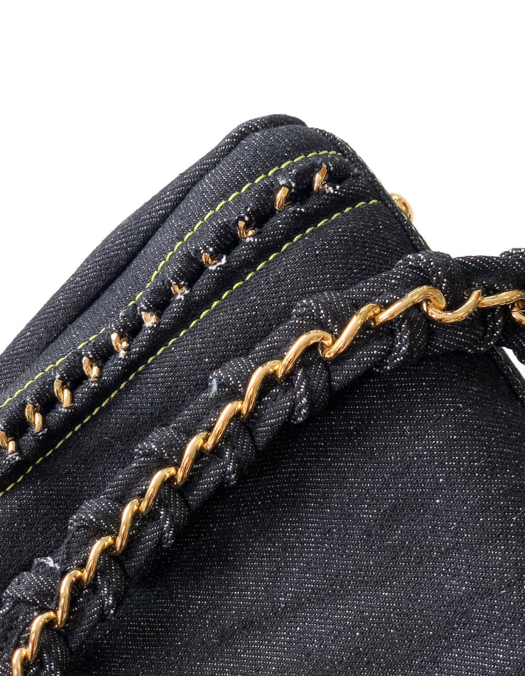 Close-up of a black denim bag featuring yellow contrast stitching, a braided black strap, and a gold-tone chain detail against a white background.