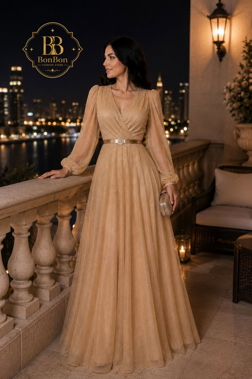 A woman wearing a floor-length champagne beige gown with long sheer sleeves and a jeweled waistband stands on a balcony at night with a city skyline in the background. The BonBon brand logo is visible in the top left corner.
