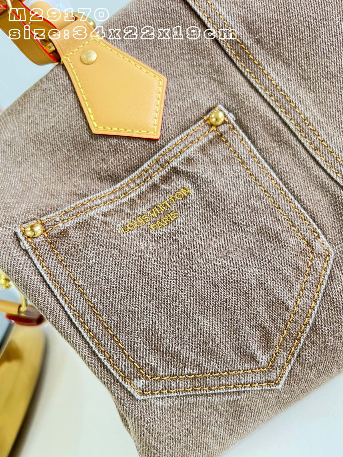Close-up of a taupe denim handbag showing the back pocket with gold contrast stitching, gold-tone hardware, and a tan leather tab. Gold 'COSTUME D'ART' branding is embroidered on the pocket.